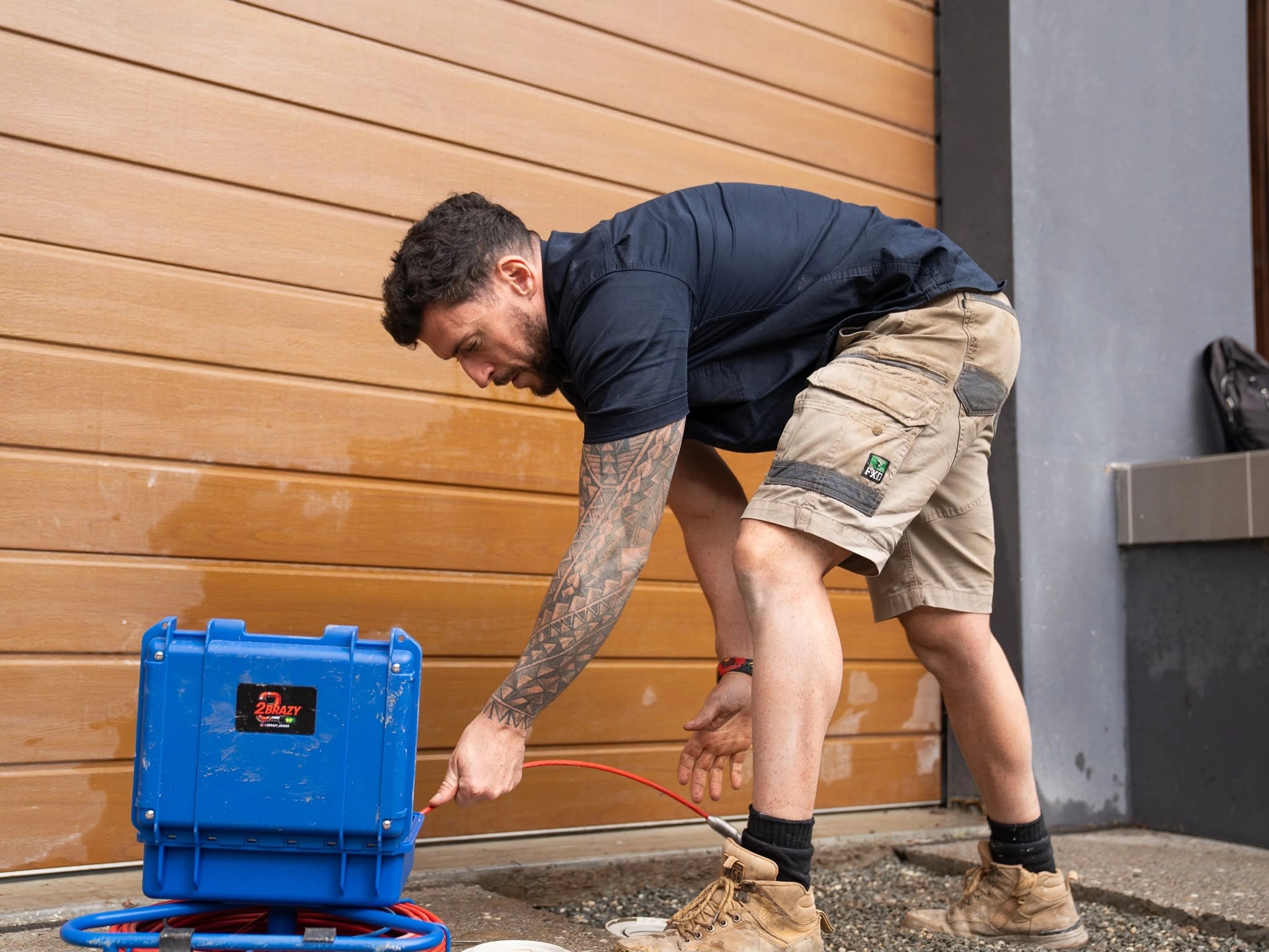 Tom Malone setting up a blue drain camera beside a timber wall